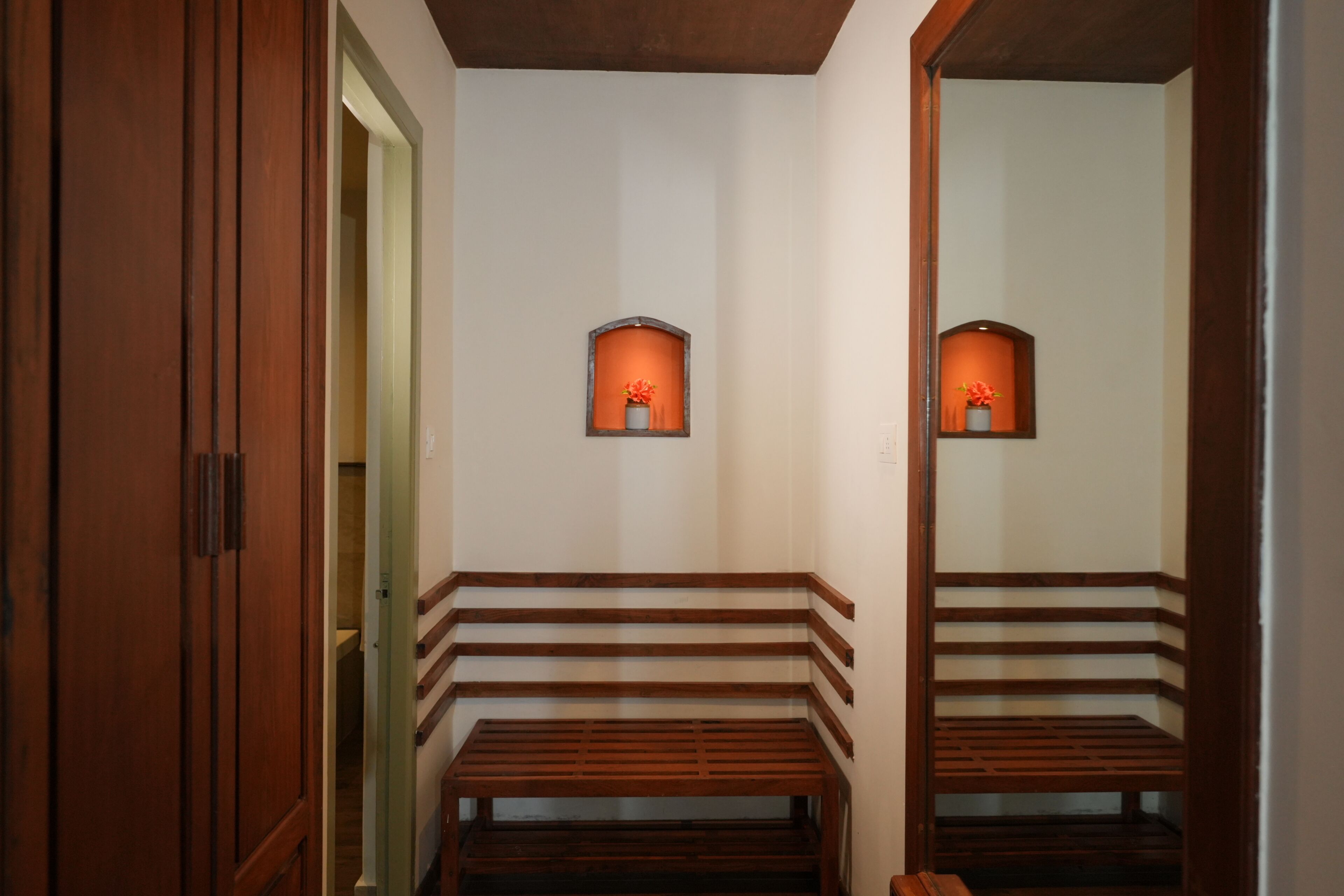 A hallway with wooden benches, a mirror reflecting the benches, and two wall-mounted sconces with orange-tinted glass.