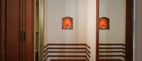 A hallway with wooden benches, a mirror reflecting the benches, and two wall-mounted sconces with orange-tinted glass.