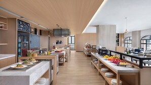 Un área de cocina moderna y bien iluminada, con alacenas de madera, una encimera larga con alimentos y un menú en una pizarra.