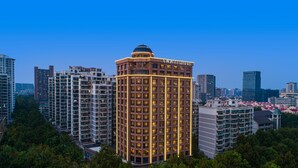 Un hotel moderno de gran altura con un diseño de esquina característico, rodeado de otros edificios y árboles.