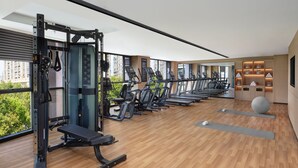 Un gimnasio moderno con diversos equipos de ejercicio, ventanas amplias y vistas al verdor.