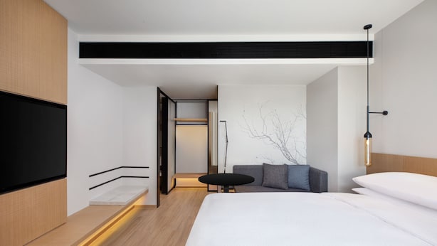 Una habitación de hotel moderna con una cama grande, una mesita redonda y una zona de estar con cojines.