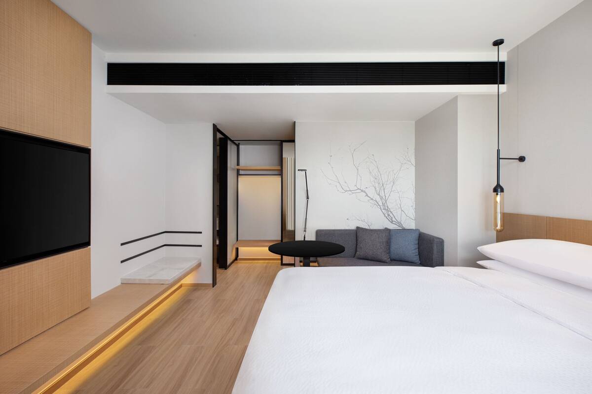 Una habitación de hotel moderna con una cama grande, una mesita redonda y una zona de estar con cojines.