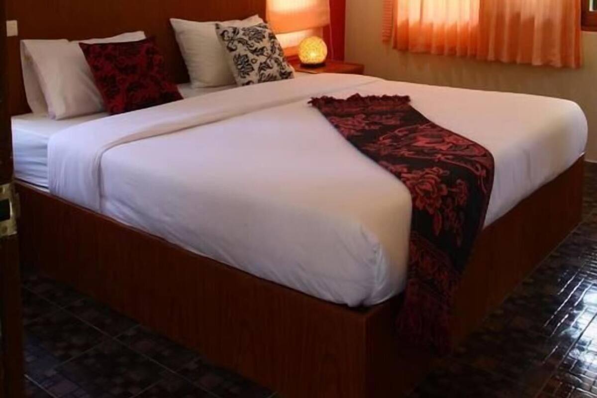 Una cama doble con cabecera de madera, aire acondicionado de pared y tres cuadros en la pared.