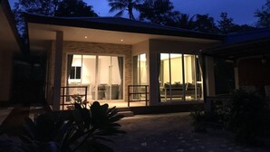 A modern house with a covered patio area, large glass doors, and a visible interior with furniture. - Phalarn Inn Resort (Koh Samui)