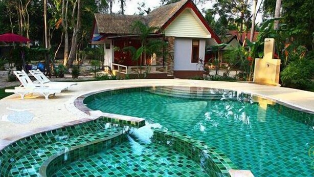 A swimming pool with a tiled edge, lounge chairs, and small buildings with thatched roofs. - Phalarn Inn Resort (Koh Samui)