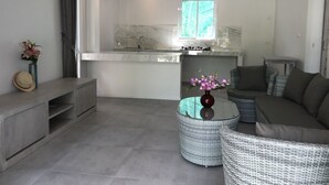 A modern living room with a grey sofa, a round wicker coffee table, and a small side table with a vase of flowers. - Phalarn Inn Resort (Koh Samui)