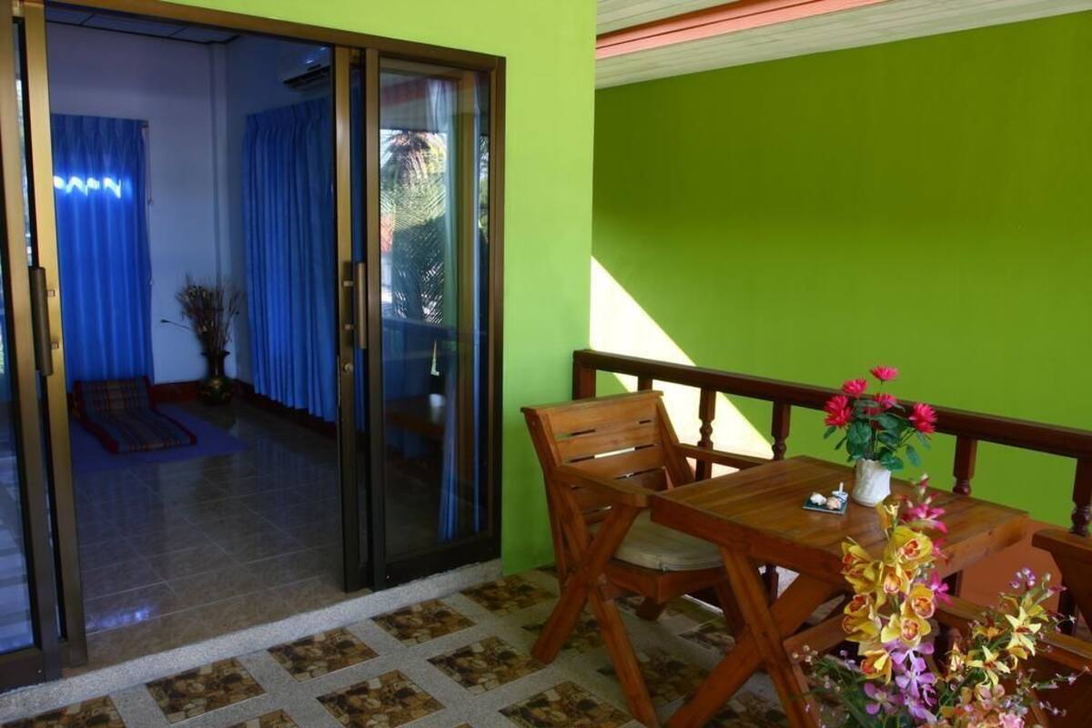 Habitación con puerta de vidrio corrediza que da a un balcón con mesa y sillas de madera, una planta en maceta y vistas al exterior.