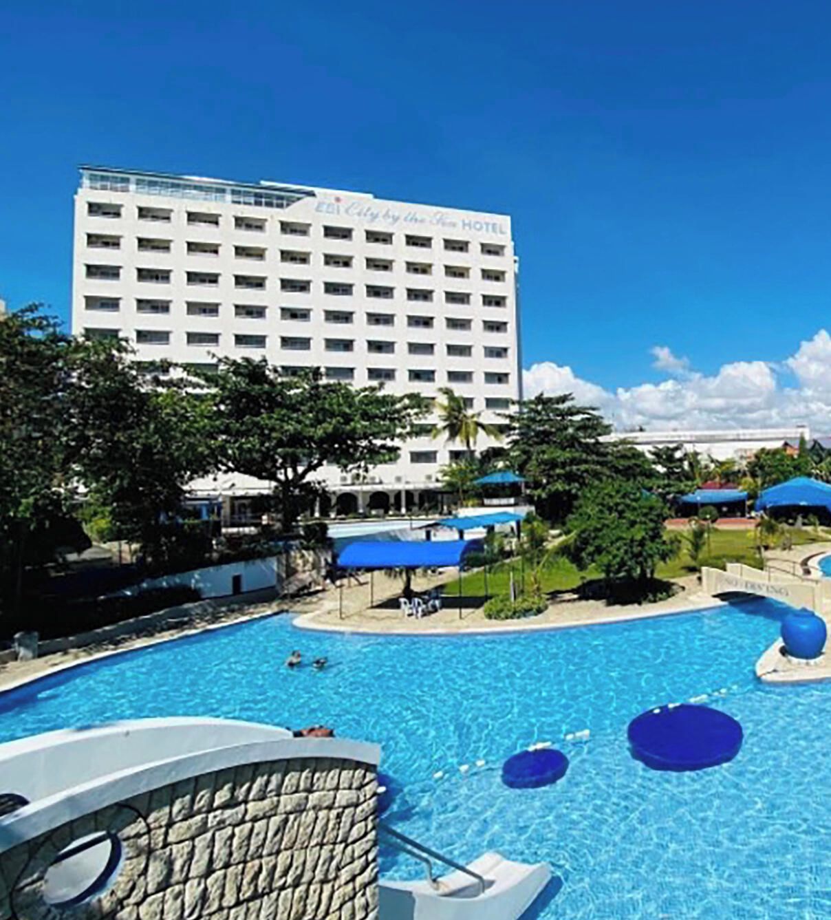 A hotel with a large pool, newly renovated rooms, and a view of the surrounding area.