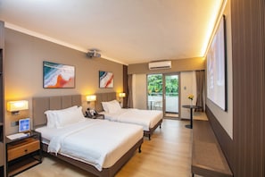 Une chambre d’hôtel avec deux lits, des lampes de chevet, un projecteur, un appareil de climatisation et un balcon donnant sur un espace verdoyant.