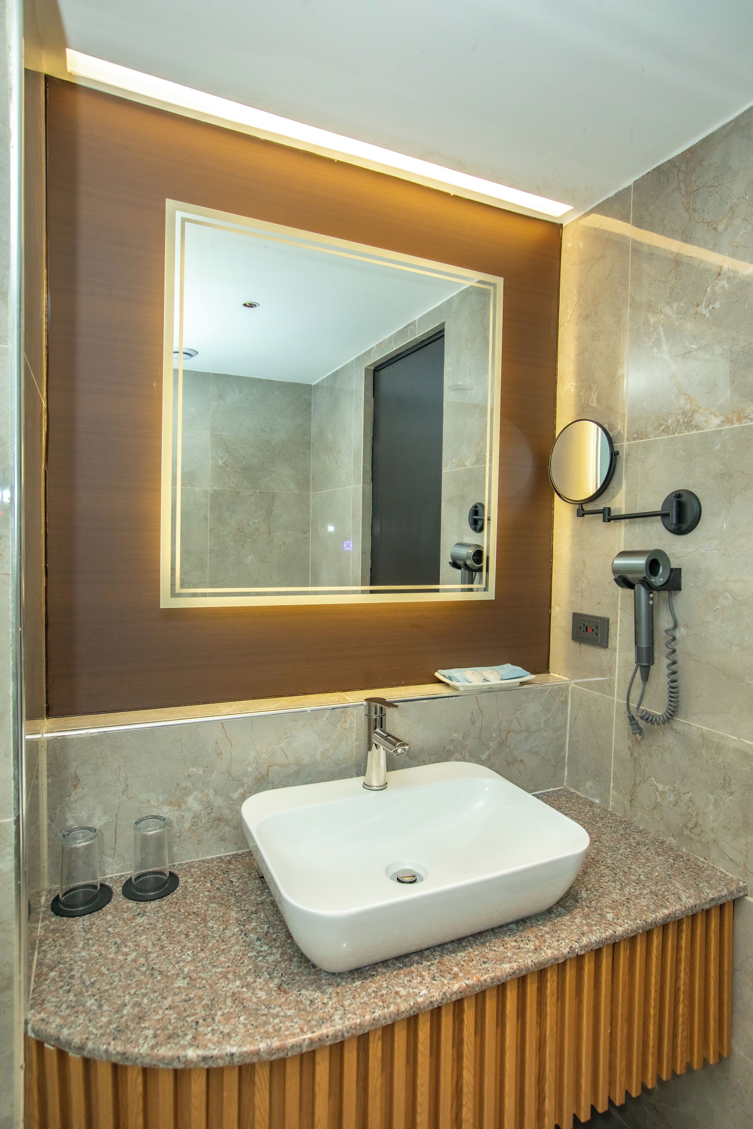 Un baño moderno con un lavamanos rectangular, un espejo y un secador de pelo montado en la pared.