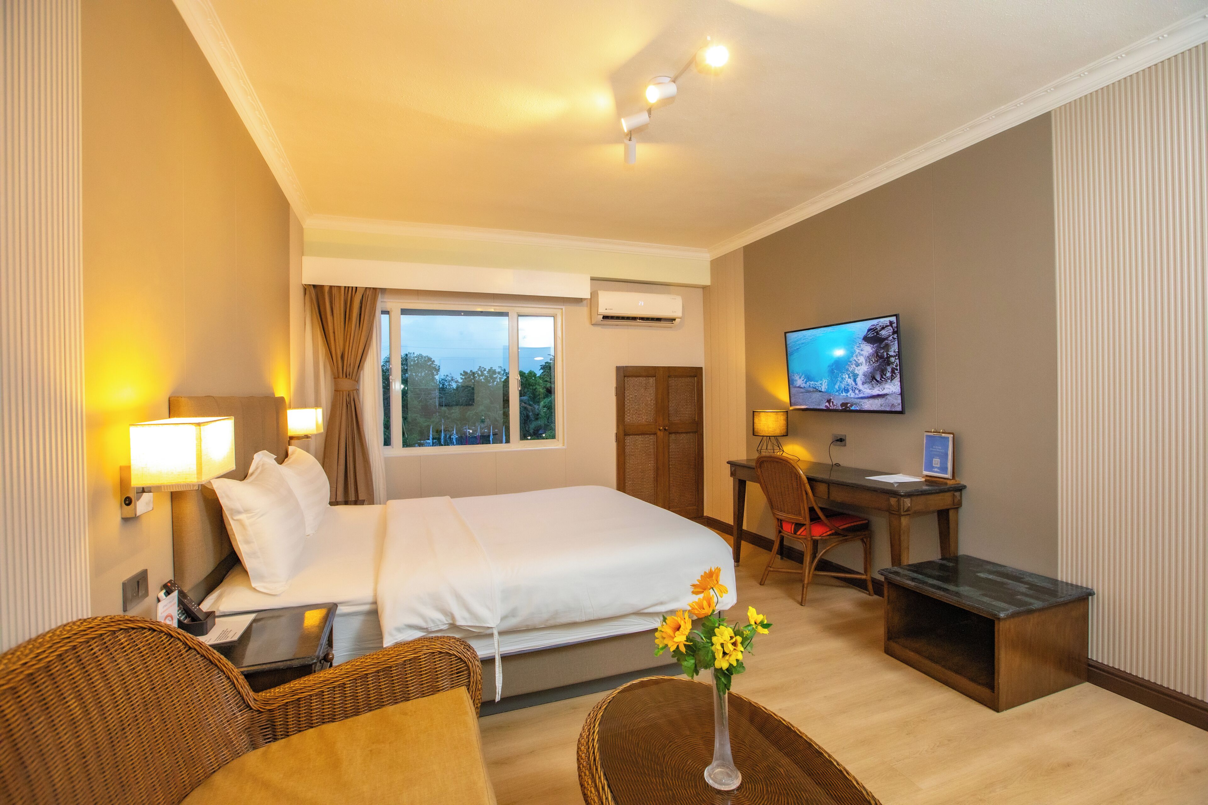 A hotel room with a bed, desk, television, and wicker furniture.