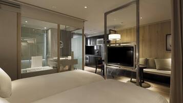 A modern hotel room with a large bed, a television, a sofa, and a glass-enclosed shower area.