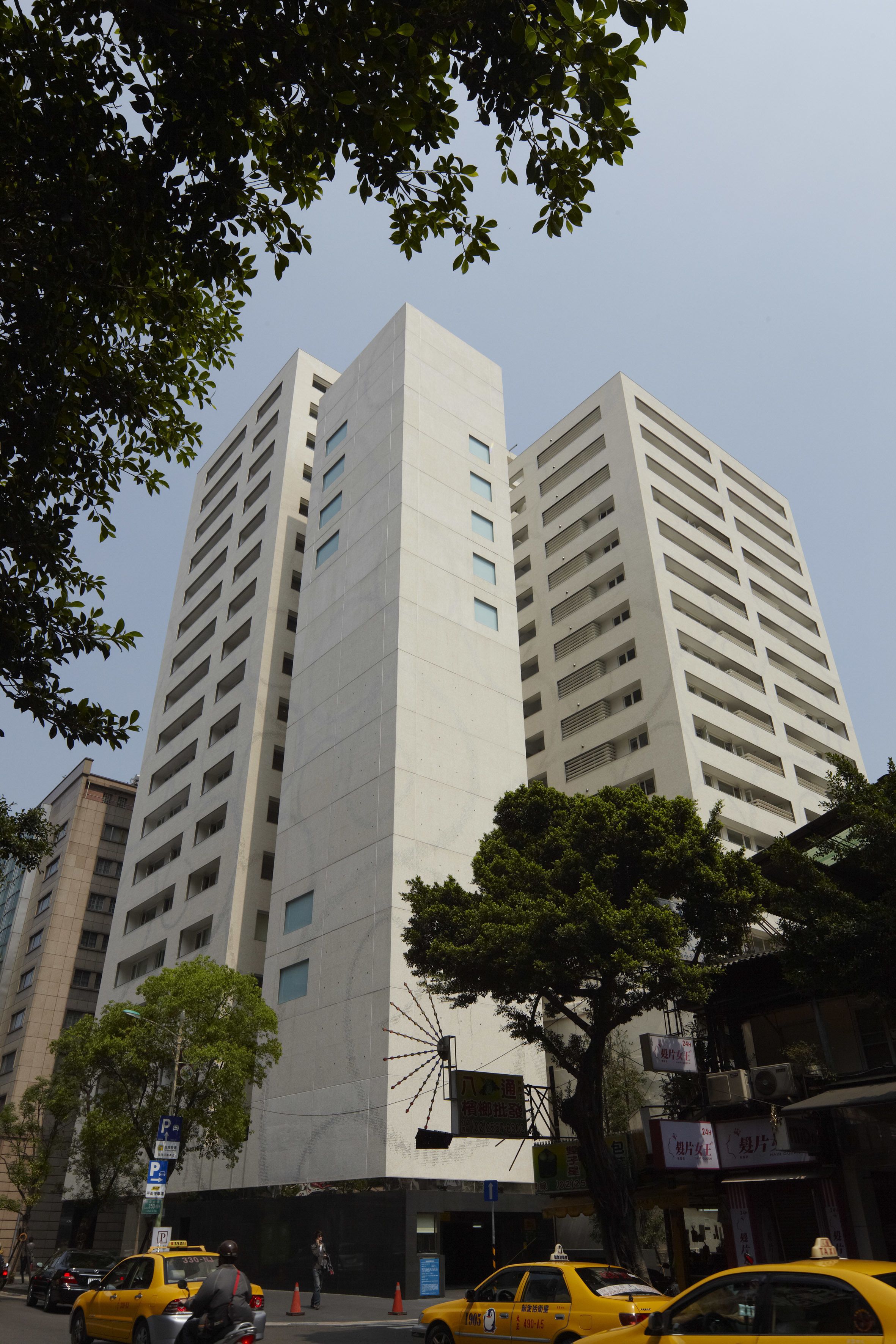 A modern high-rise building with multiple floors, large windows, and a parking sign visible in the foreground.