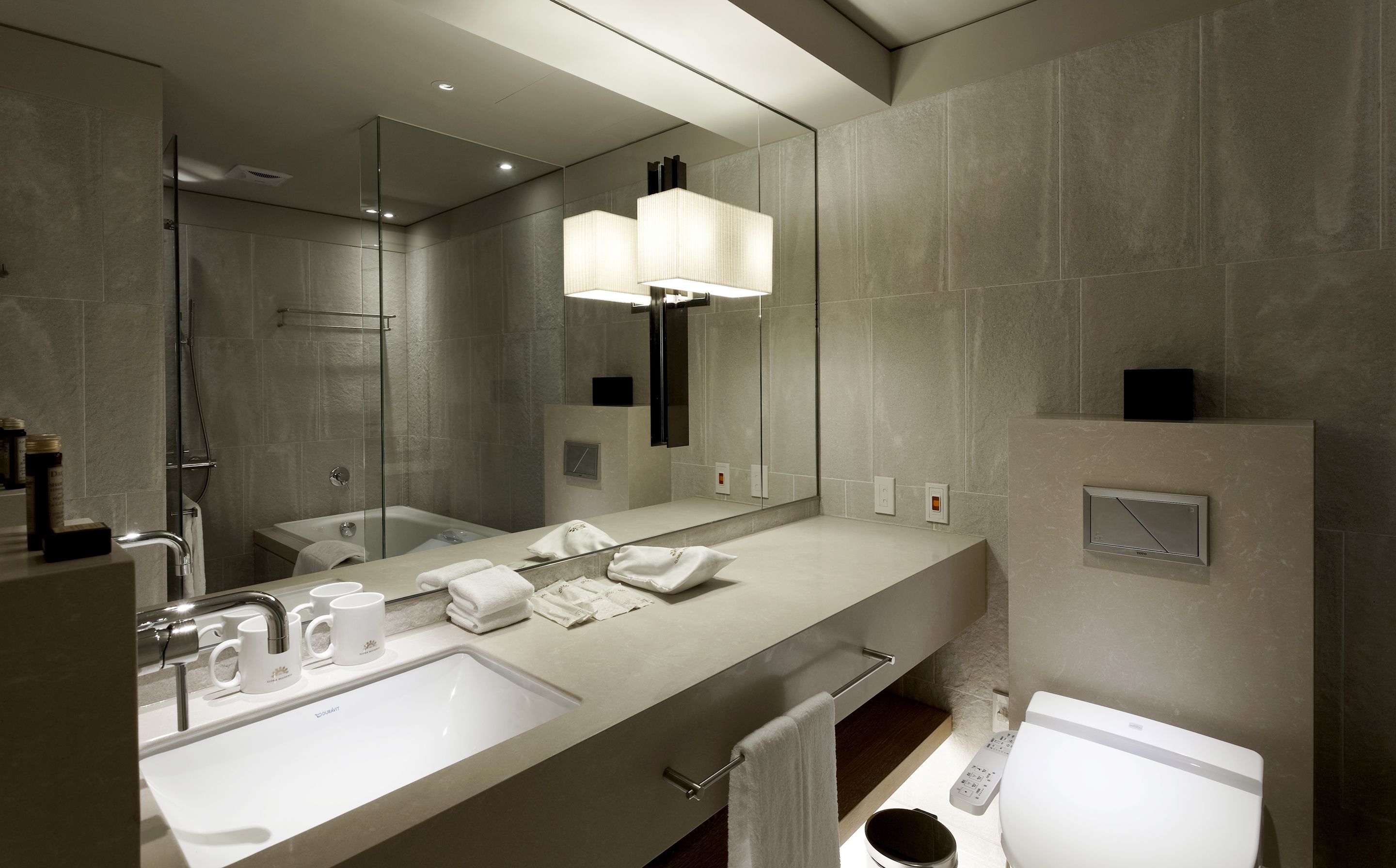 A modern bathroom with a large mirror, two sinks, a shower, and a toilet.
