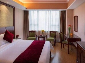 A hotel room with a large bed, a desk with two chairs, a small table with flowers, and a large window with curtains. - Vienna Hotel Pinghu Plaza Branch (Shenzhen)