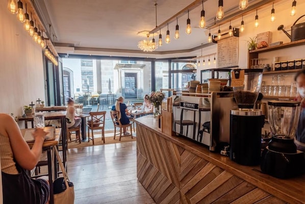 A café interior with wooden furniture, a bar counter, and a view of the street outside. - Beethoven Hotel Dreesen - furnished by BoConcept (Bonn)