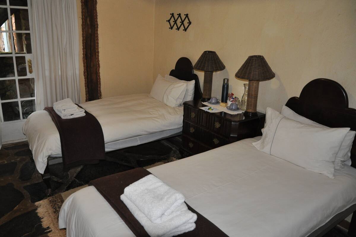 A hotel room with two beds, a dresser, a lamp, and a window with curtains.