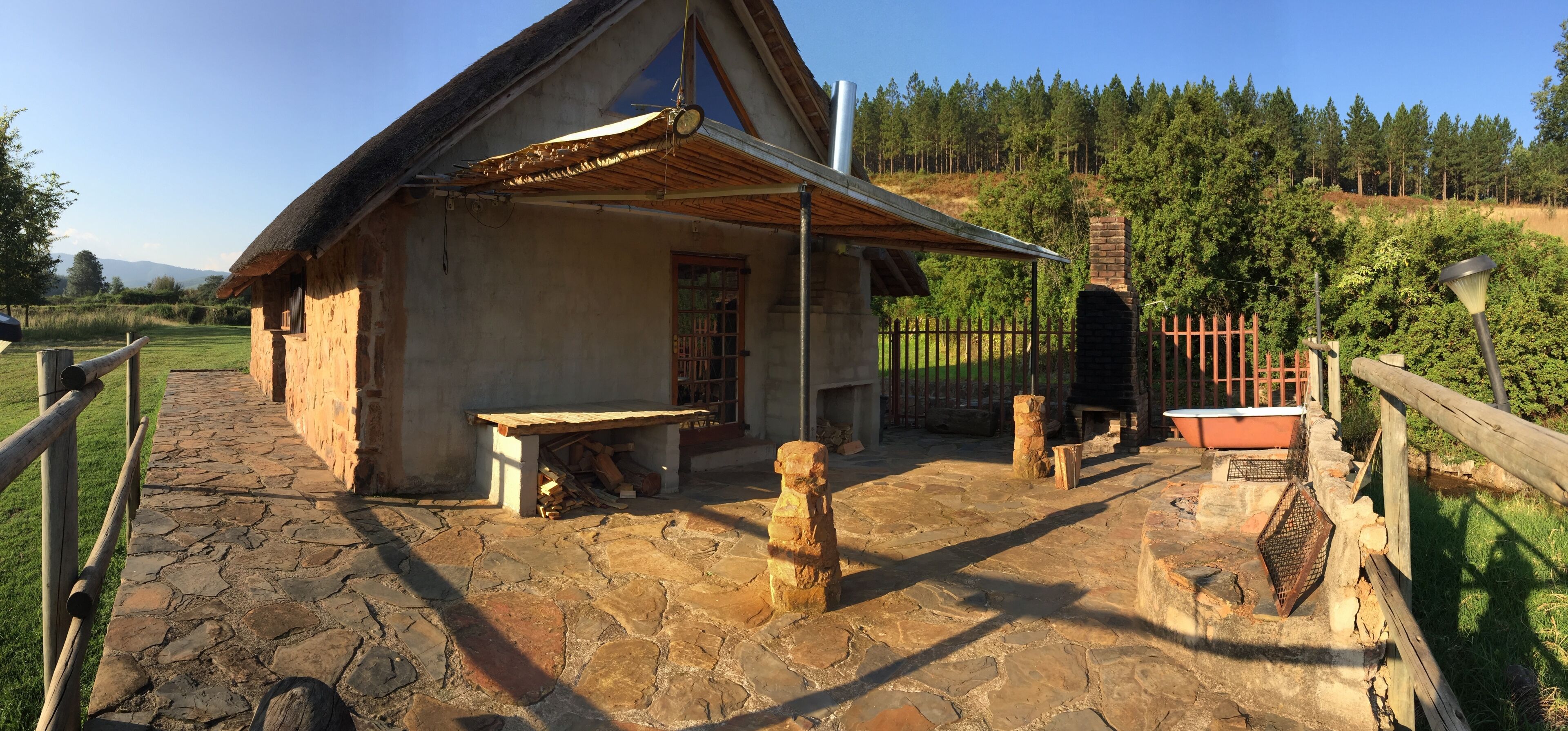 Um edifício rústico de pedra com telhado de palha, chaminé e cerca de madeira.