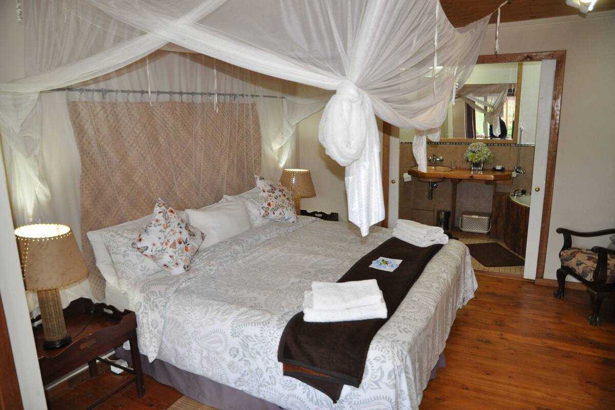 A bedroom with a canopy bed, bedside lamps, a vanity with a mirror, and a wooden floor.