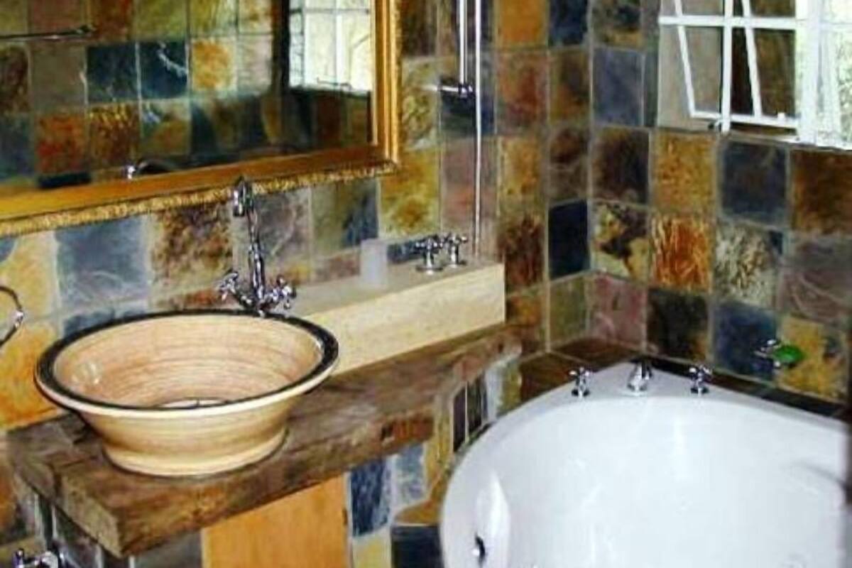 A bathroom with a large bathtub, a wooden vanity with a bowl sink, and a mirror with a stained glass window.