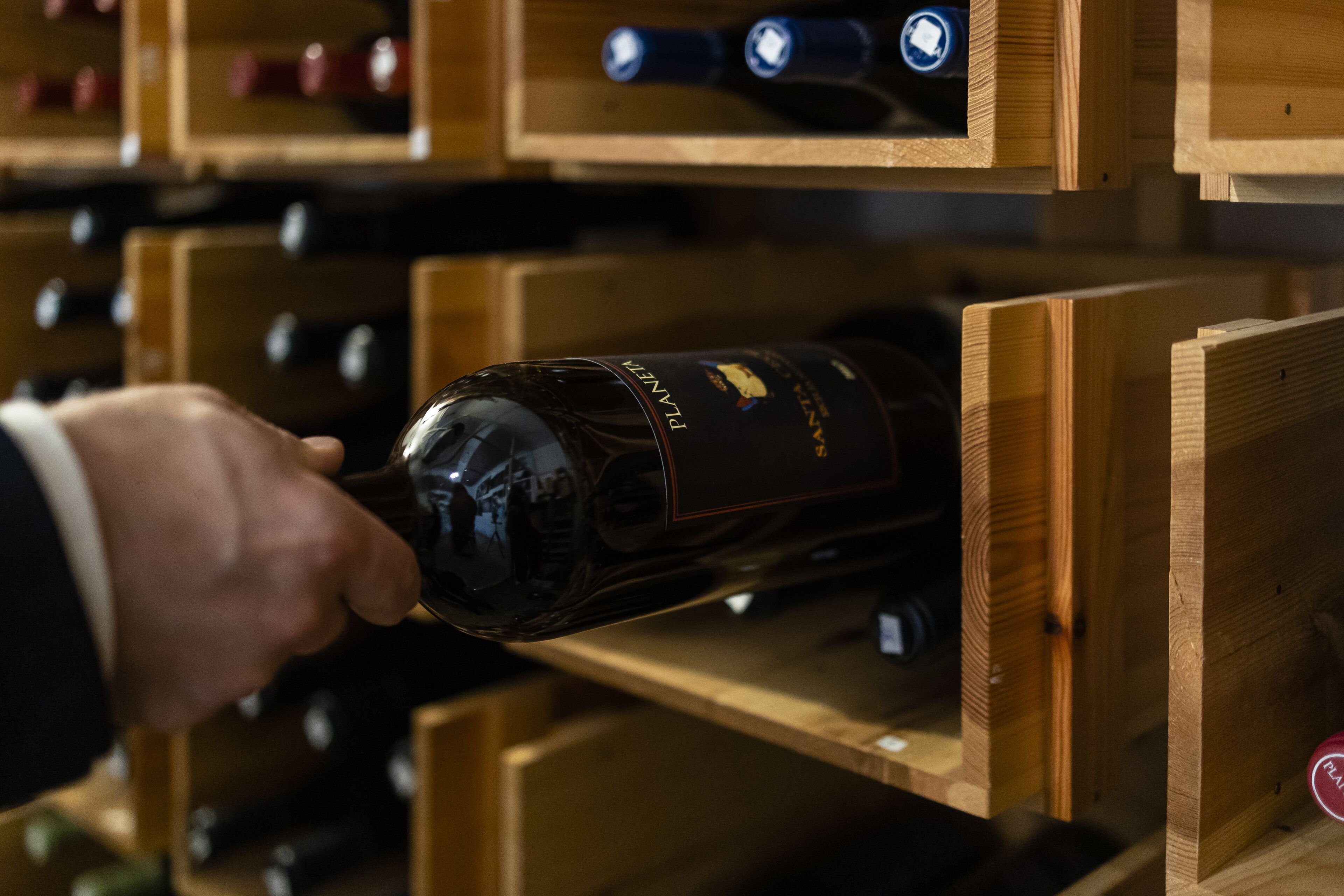 A hand reaching for a bottle in a wooden wine rack.