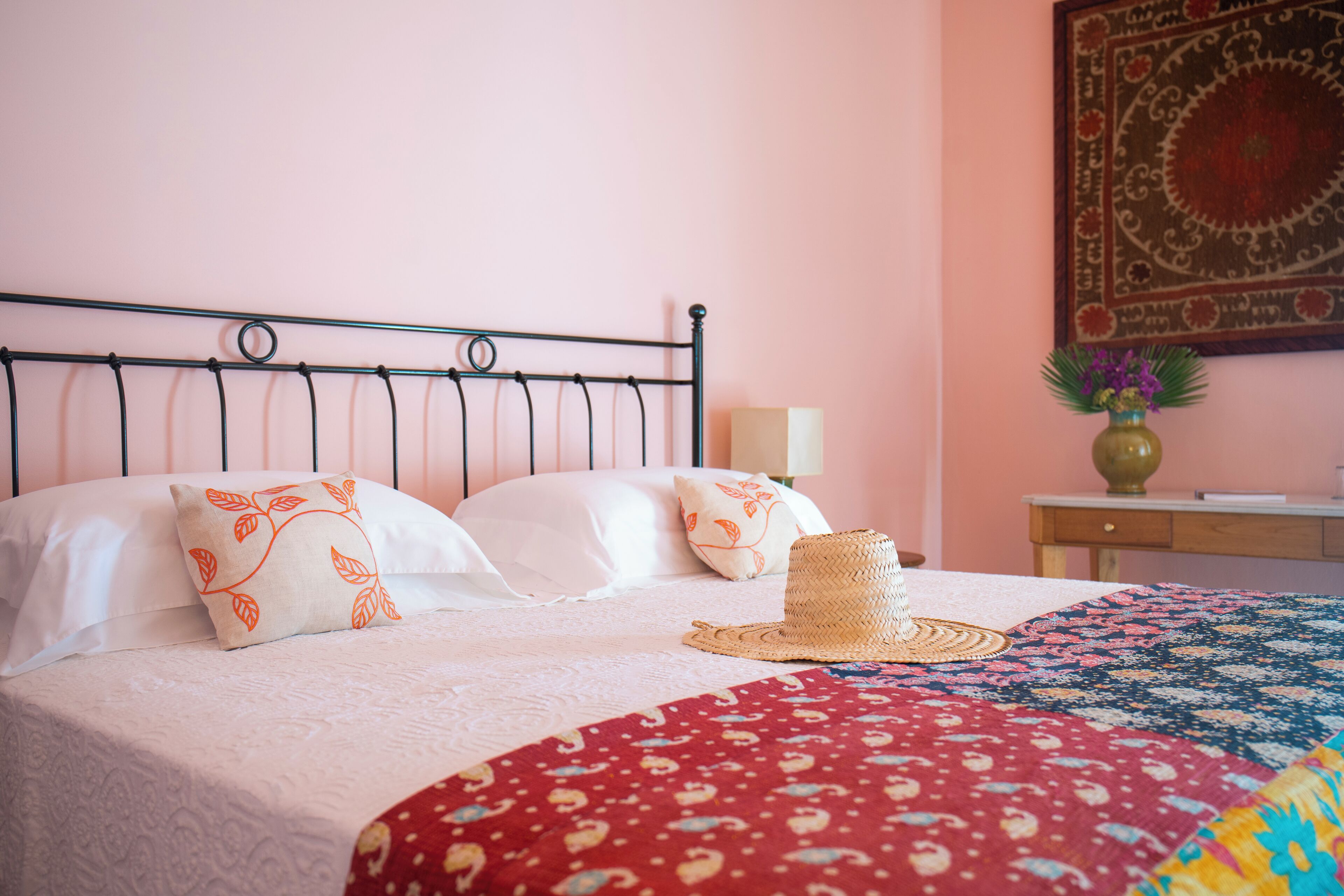 A neatly made bed with a patterned bedspread, two pillows with leaf designs, and a straw hat on the bed.