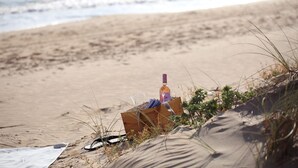A beach scene with a wooden crate containing a bottle, glasses, and a notebook. - La Foresteria Planeta Estate (Menfi)
