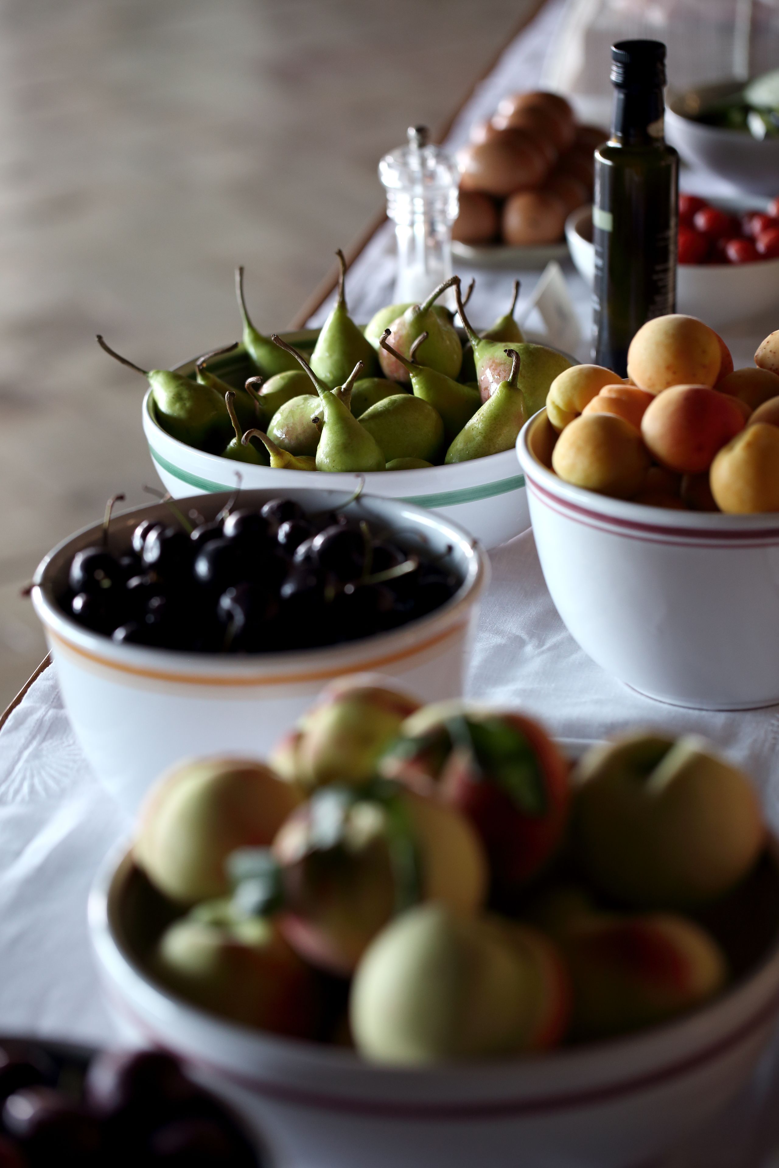 Una mesa con tazones de frutas variadas, como peras, cerezas y manzanas.
