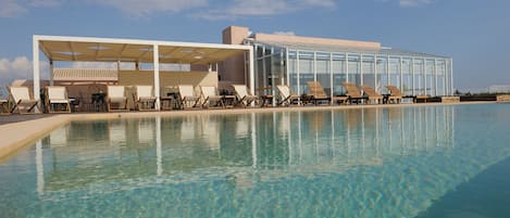 Una piscina al aire libre, sombrillas, sillones reclinables de piscina