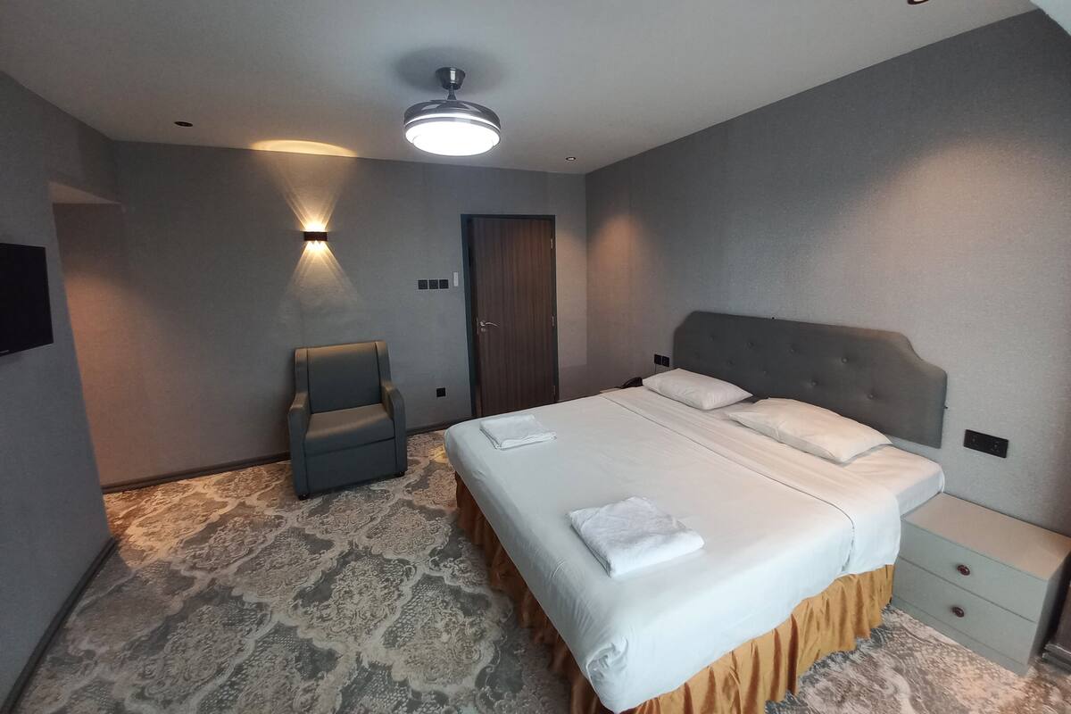 A hotel room with a large bed, a chair, a desk, and a ceiling fan.