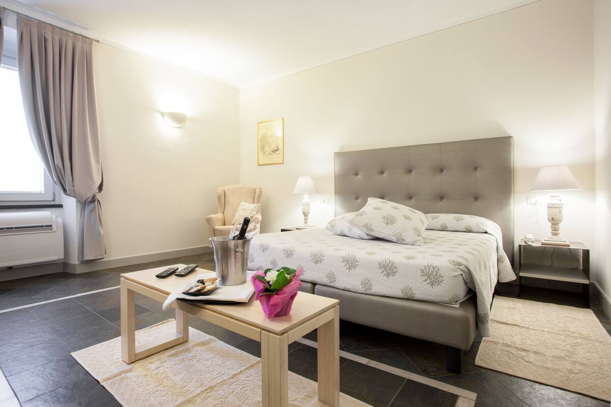 Ein Hotelzimmer mit Bett, Nachttisch, Stuhl, Lampe und einem Fenster mit Vorhängen.