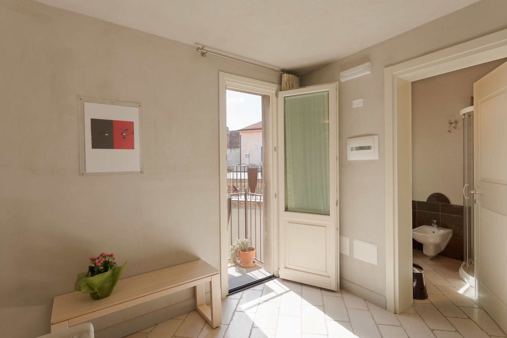 Un pasillo con un banco, una puerta que da a un balcón y un baño con bidé.