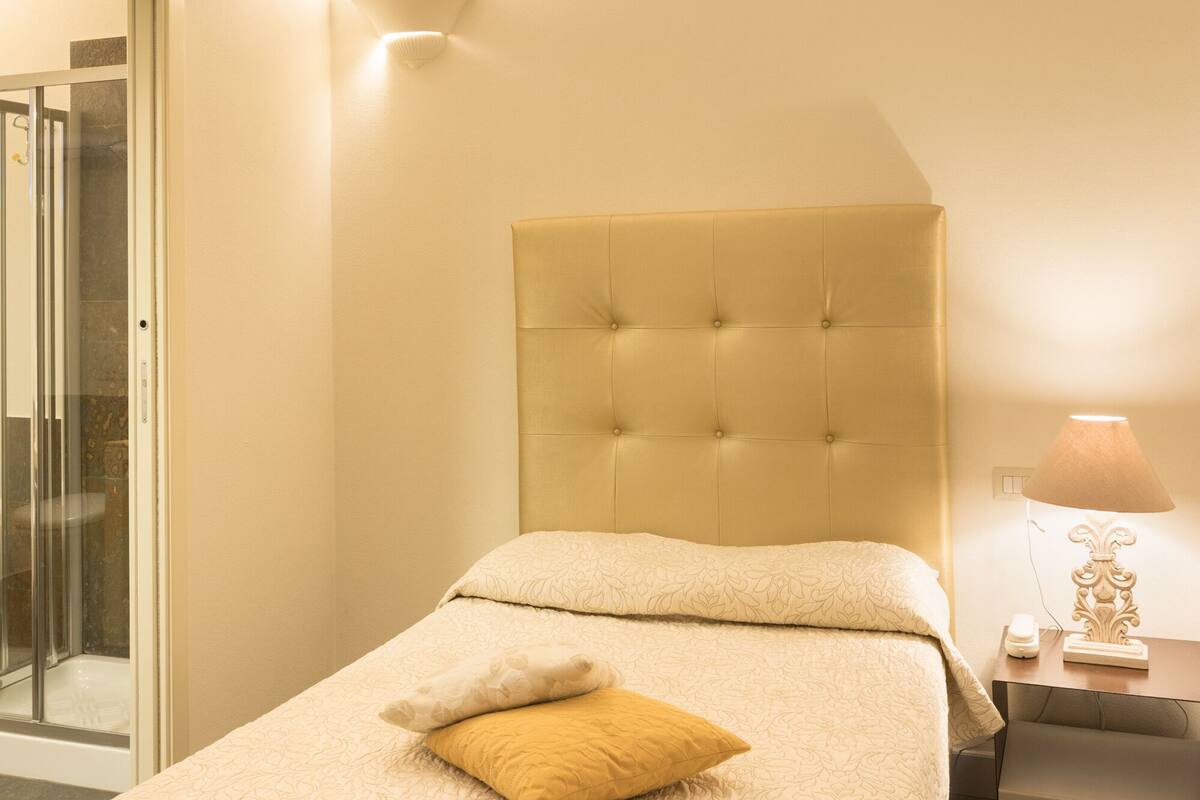 Ein Hotelzimmer mit einem Bett, einem Nachttisch, einer Lampe und einer Tür zu einem Badezimmer.