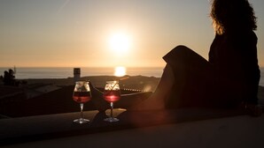 Una persona sentada junto a una ventana con vista a la puesta de sol sobre el océano.