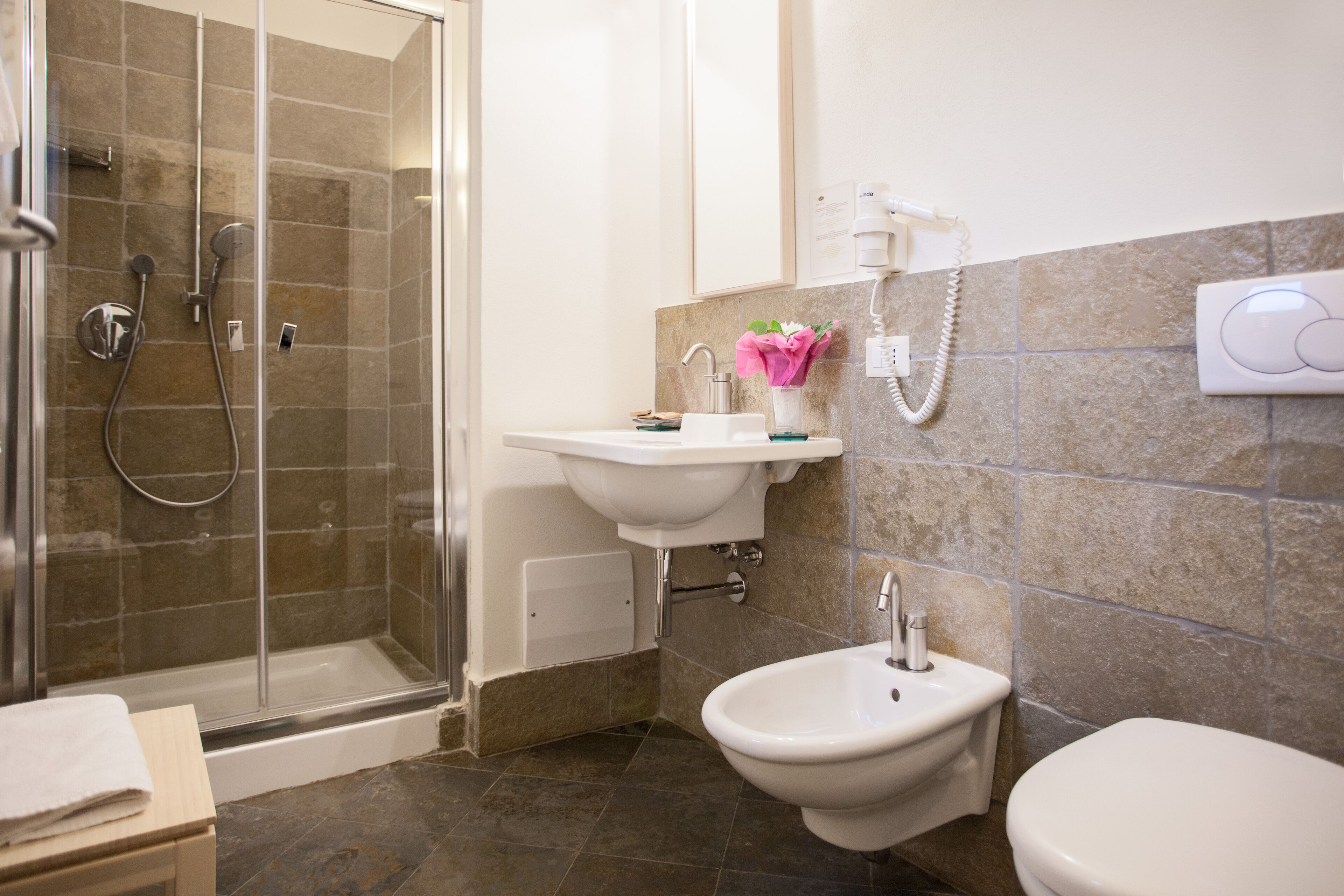 A bathroom with a glass-enclosed shower, a sink, a bidet, and a toilet.