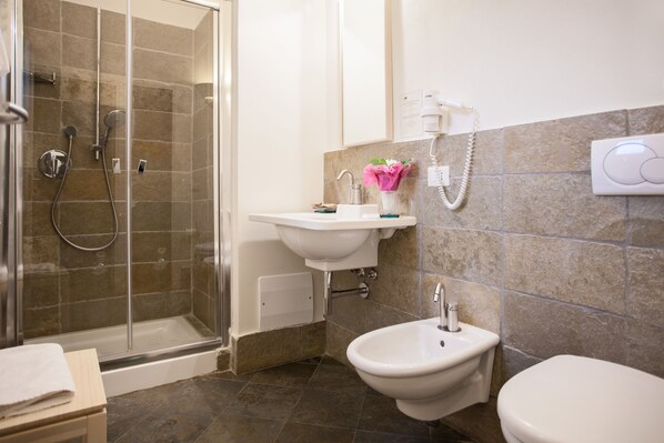 A bathroom with a glass-enclosed shower, a sink, a bidet, and a toilet.