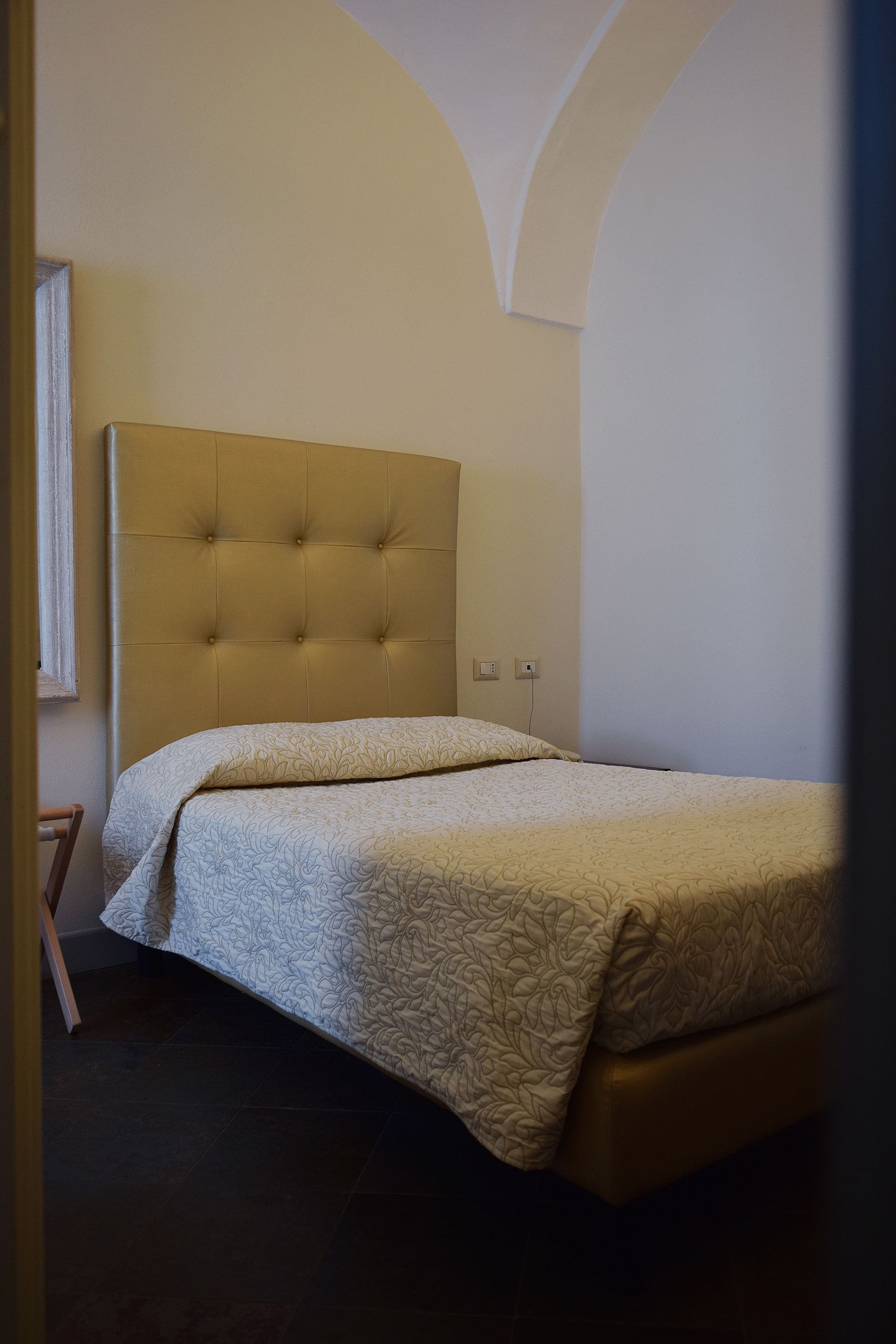 A bedroom with a tufted headboard, a bed with patterned bedding, and a tiled floor.