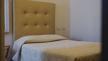 A bedroom with a tufted headboard, a bed with patterned bedding, and a tiled floor.
