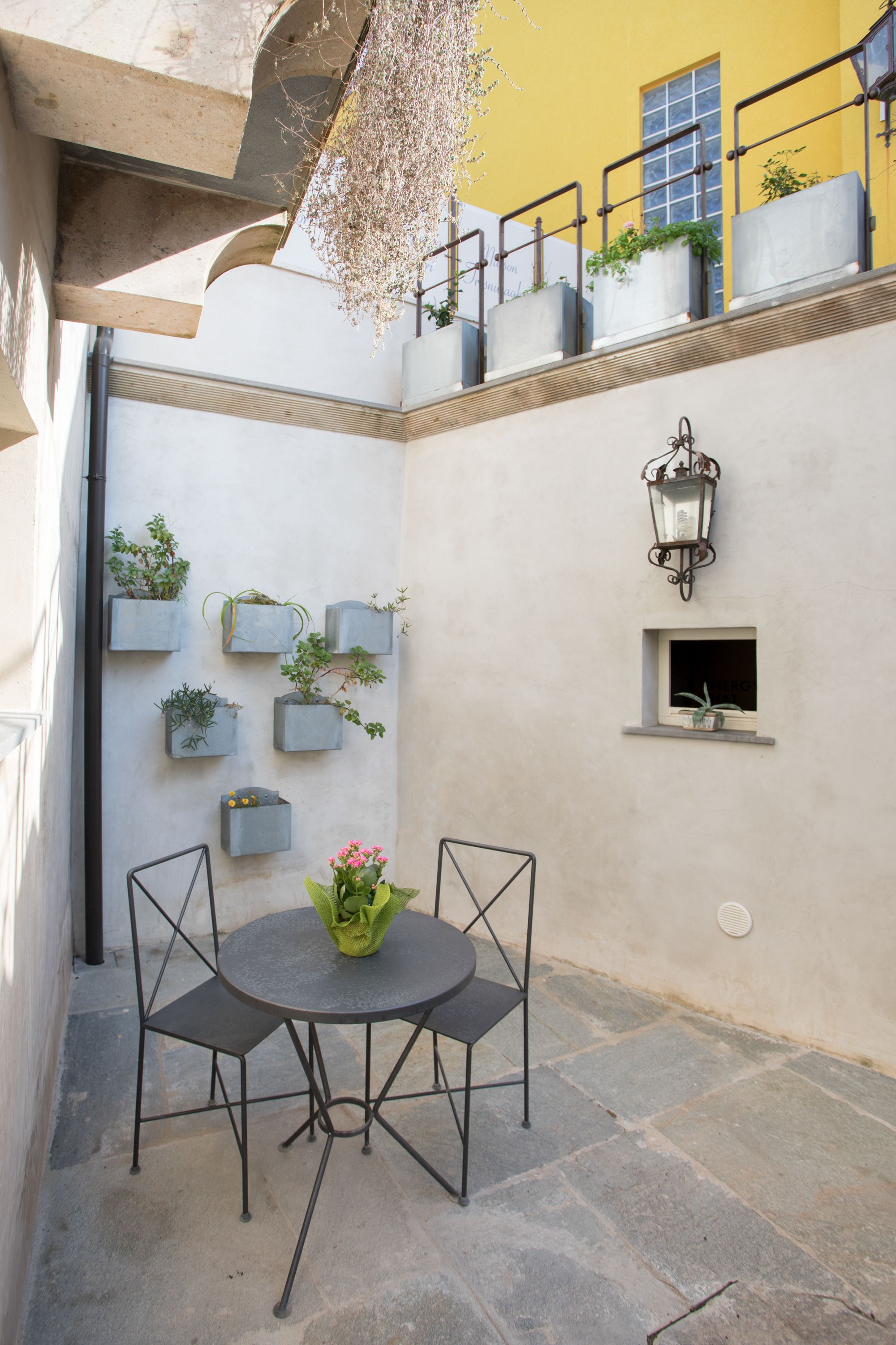 A courtyard with a round table and chairs, potted plants, and a lantern.