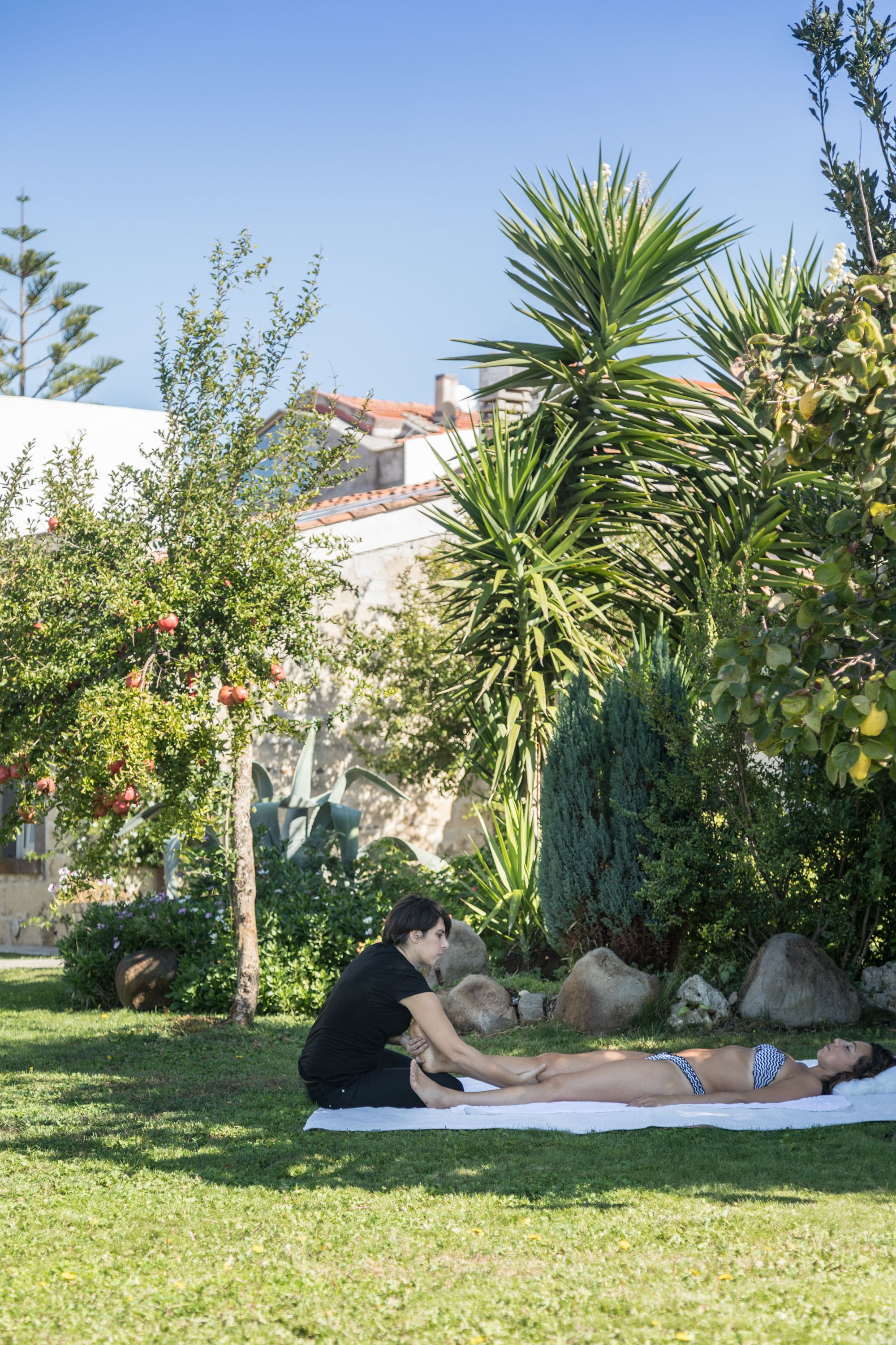 A person lying on a towel in a grassy area with trees and a building in the background.