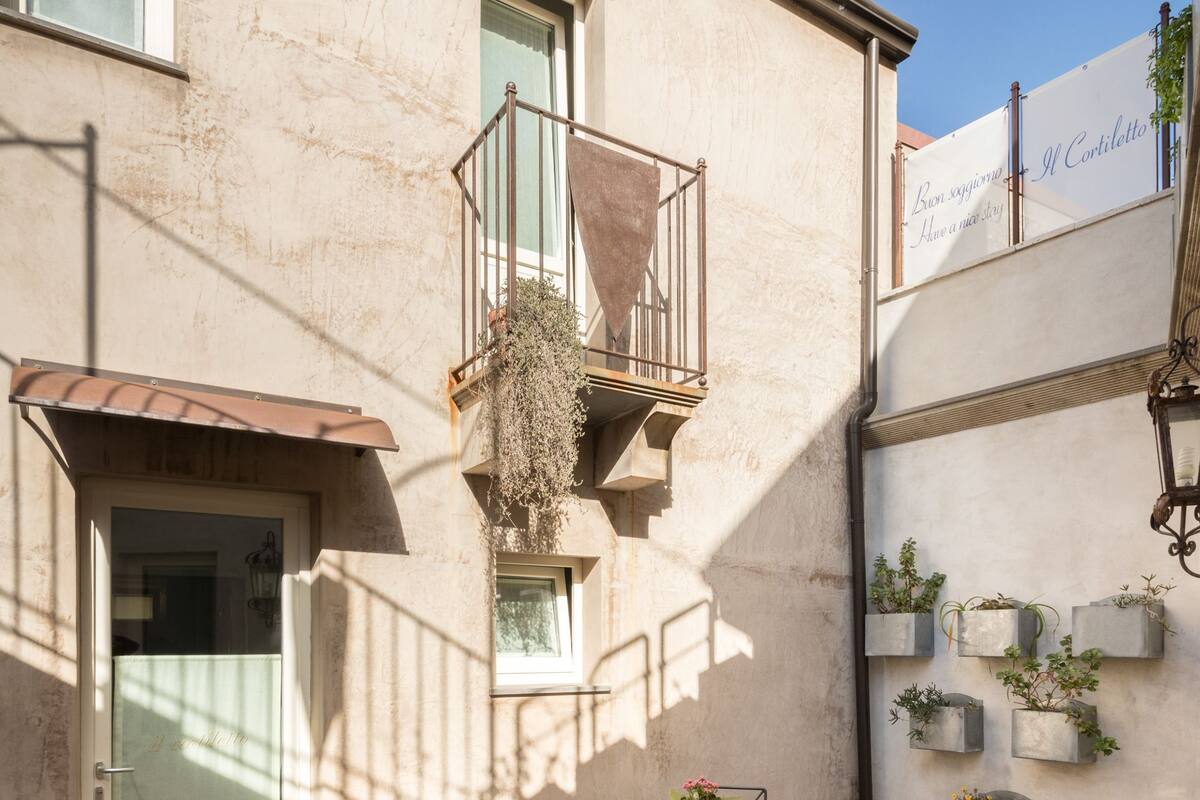 Ein Gebäude mit sandfarbener Fassade, einem Balkon mit Metallgeländer, einer Tür mit Glasfenster und einem kleinen Tisch mit Stühlen.