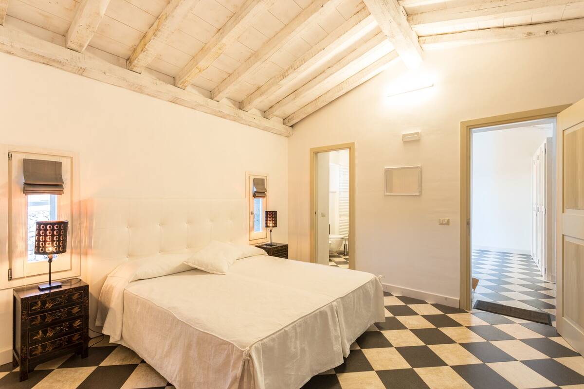 Ein Schlafzimmer mit Bett, Nachttisch, Lampe, Spiegel und einem karierten Boden.