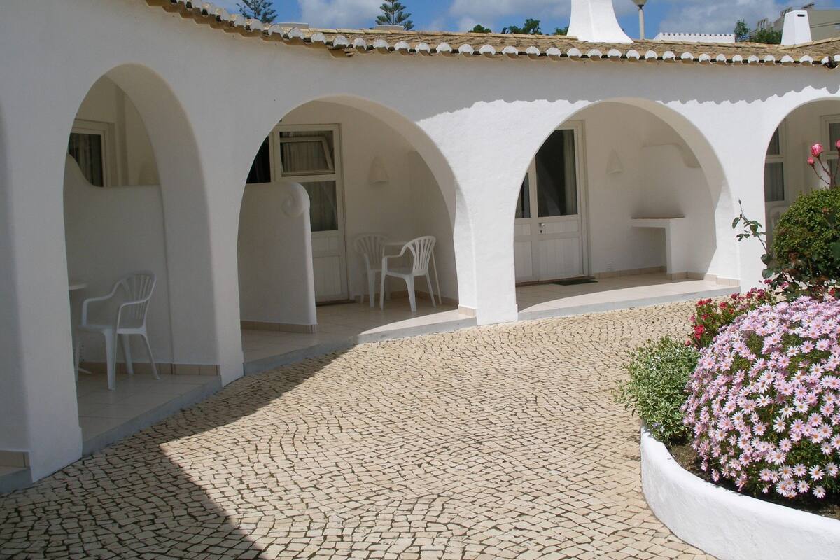 Une cour intérieure agrémentée d’arches blanches, d’un sol carrelé et d’un parterre de fleurs roses.