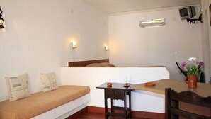 A small, cozy room with a bed, a table, and a chair. There is a window with an air conditioning unit above it.