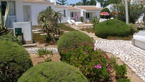 A courtyard with neatly trimmed hedges, a cobblestone pathway, and a white building with a tiled roof.