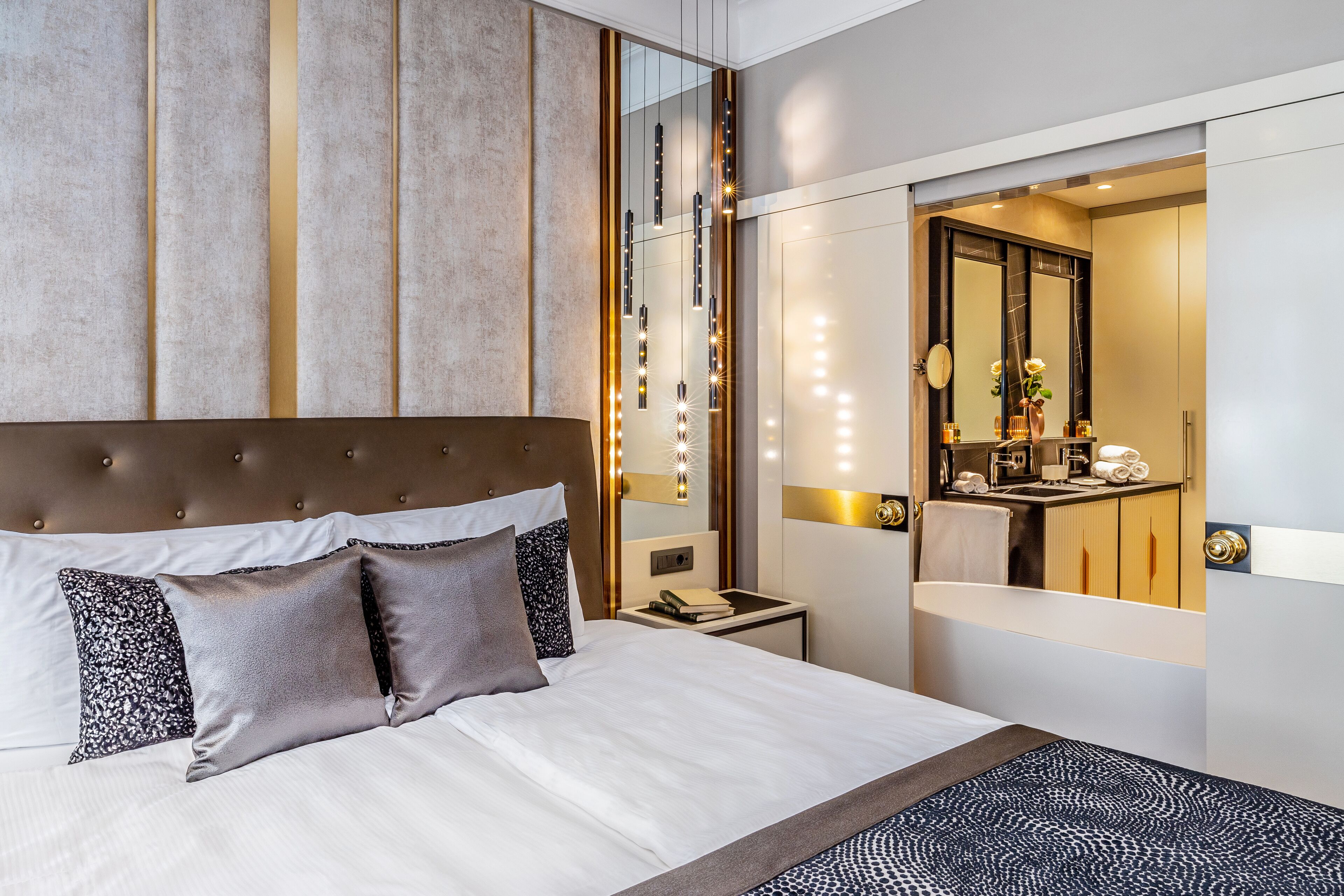 A modern hotel room with a large bed, a bedside table, a mirror, and a bathroom visible through an open door.