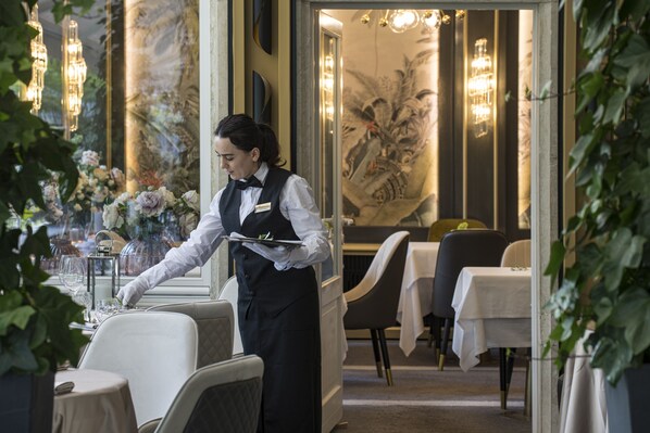 A waiter in a formal uniform serving a table in a restaurant with elegant decor and traditional Chinese artwork. - VILLA EDEN - The Private Retreat (Merano)