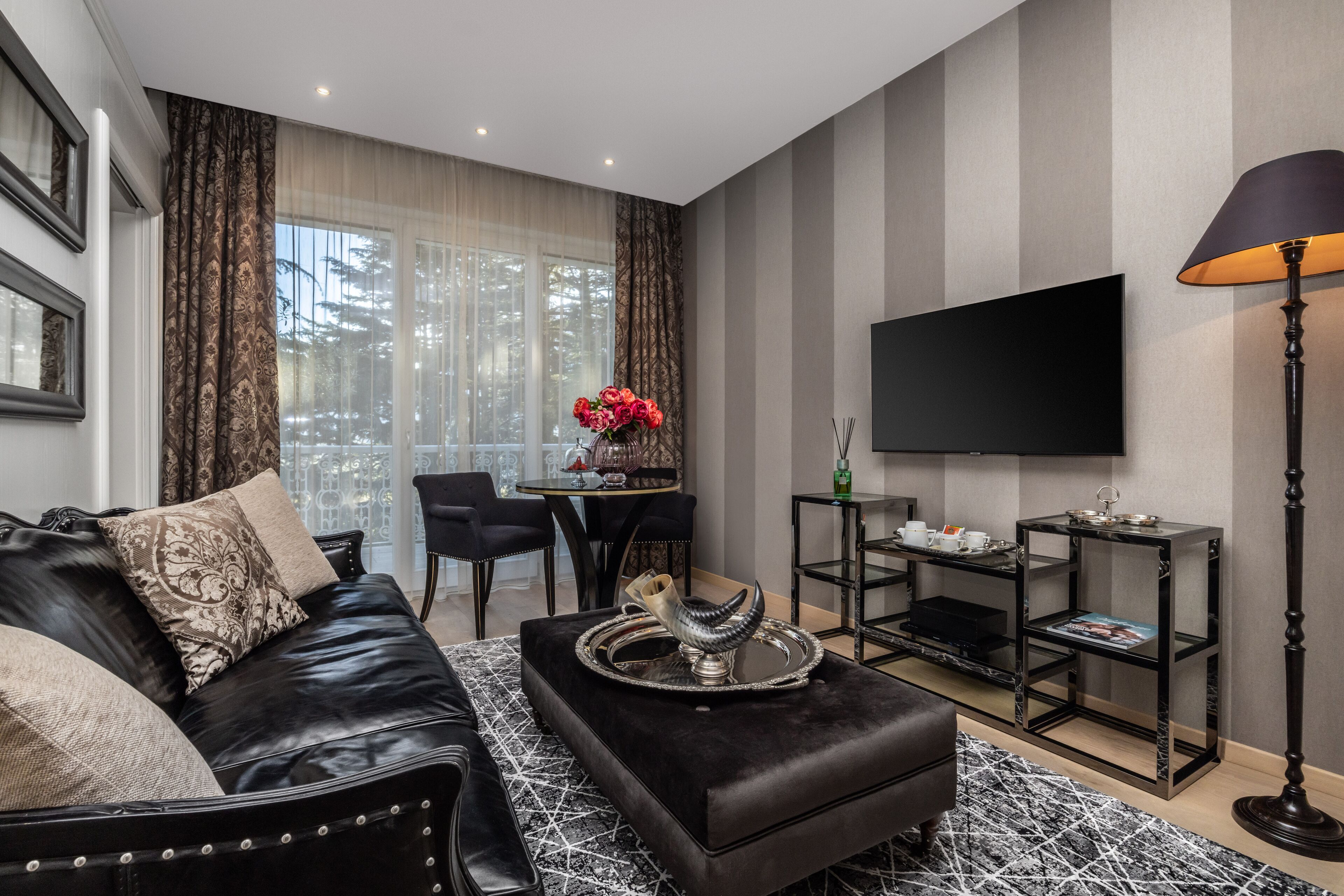 Una sala de estar moderna con un sofá de cuero negro, una mesa de centro con objetos decorativos, un televisor de pantalla plana y una lámpara de pie.
