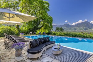 A poolside area with a curved black sofa, lounge chairs, and a pergola with a canopy.